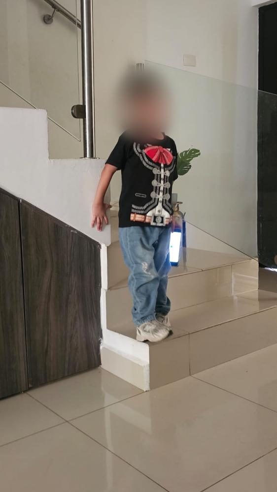 Niño con camiseta de charro bajando la escalera de su casa; el rostro está difuminado